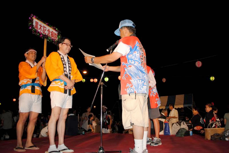 大会終了後の夜に表彰を受けるオレンジの法被を着た男性
