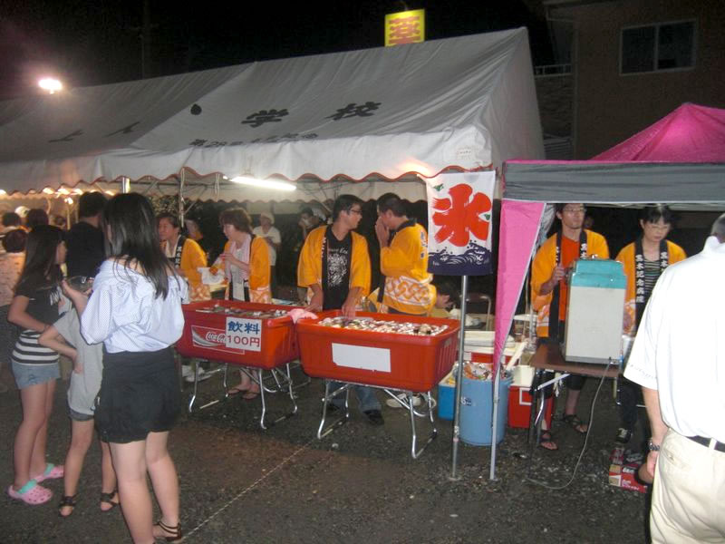 盆踊り大会の出店で飲み物を販売するオレンジの法被を着た複数名の黒木記念病院スタッフ