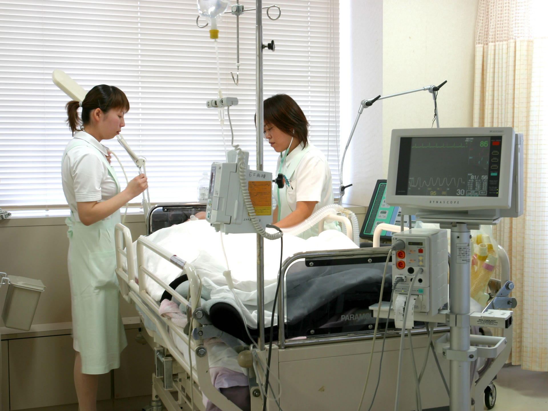 HCU（高度医療室）で機器に囲まれて寝ている患者と看護をする看護師